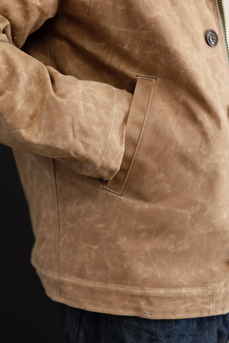 Close-up of the side profile and hand pocket of a tan canvas work jacket on a male model.