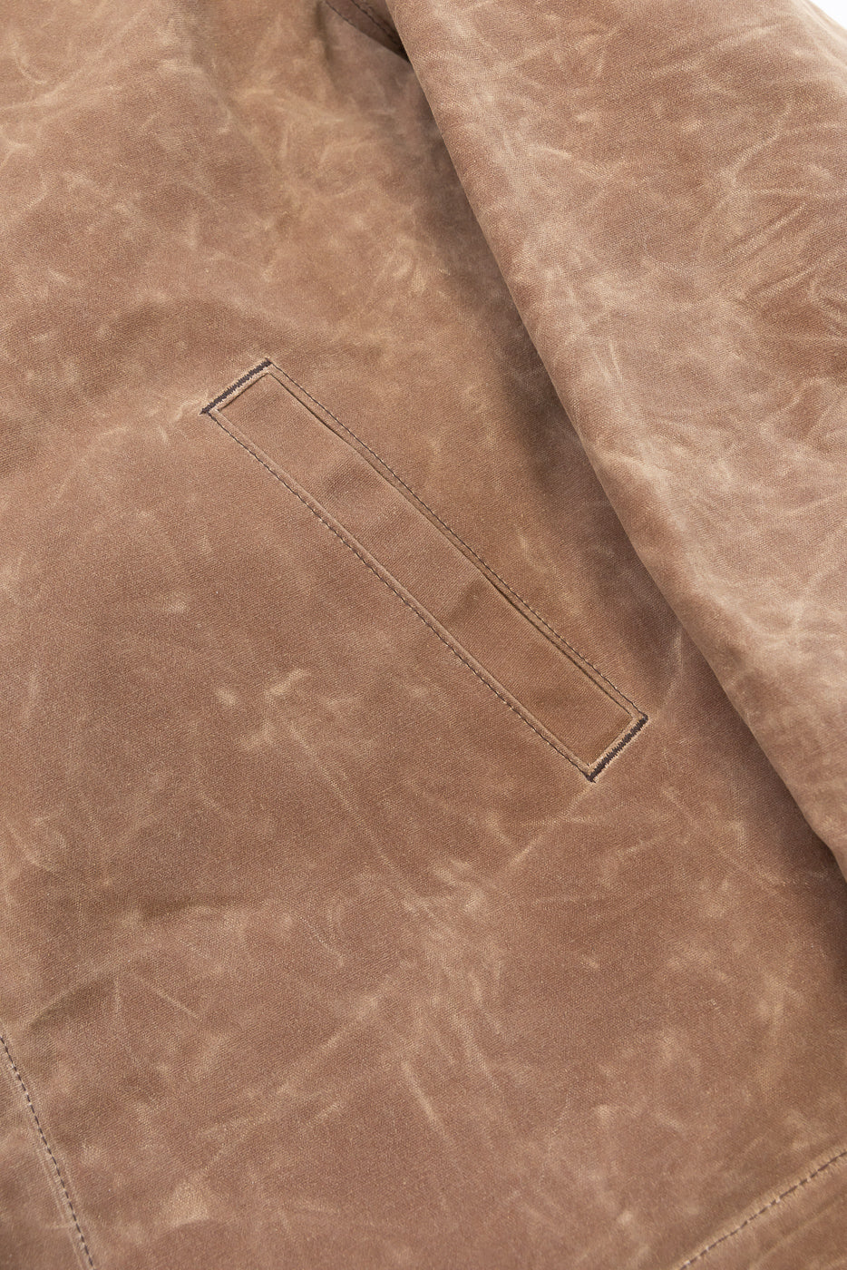 Close-up detail of the back of a brown distressed leather jacket showing a welt pocket.
