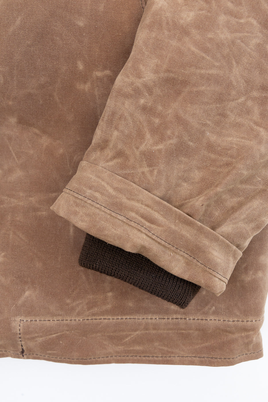 Close-up of the cuff and hem of a brown waxed canvas jacket, showing the ribbed knit sleeve cuff.