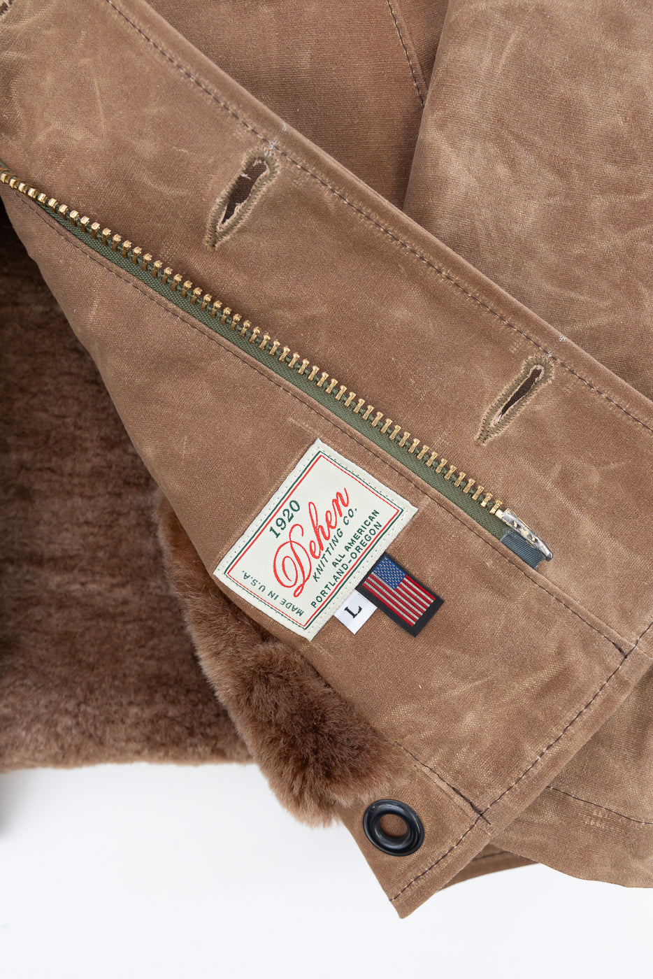 Close-up of the interior front of a brown canvas jacket showing a Dehen Knitting Co. tag and zipper.
