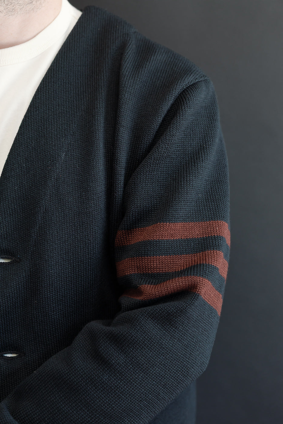 Close-up of the left sleeve on a navy blue knit cardigan featuring three orange stripes.