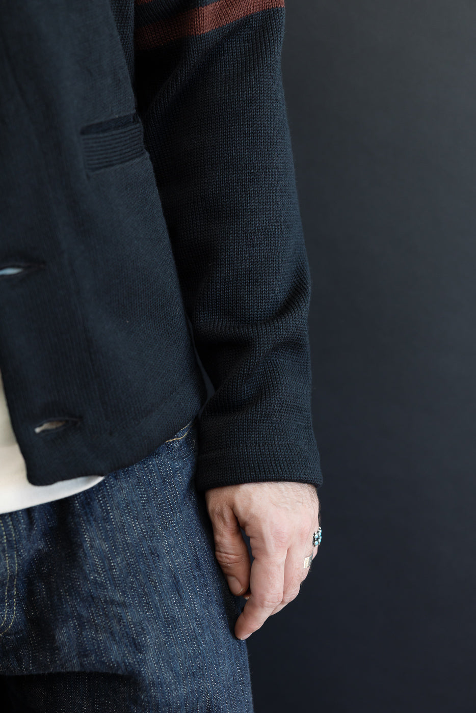 Close-up side view of a male model wearing a dark navy knit cardigan and denim jeans.