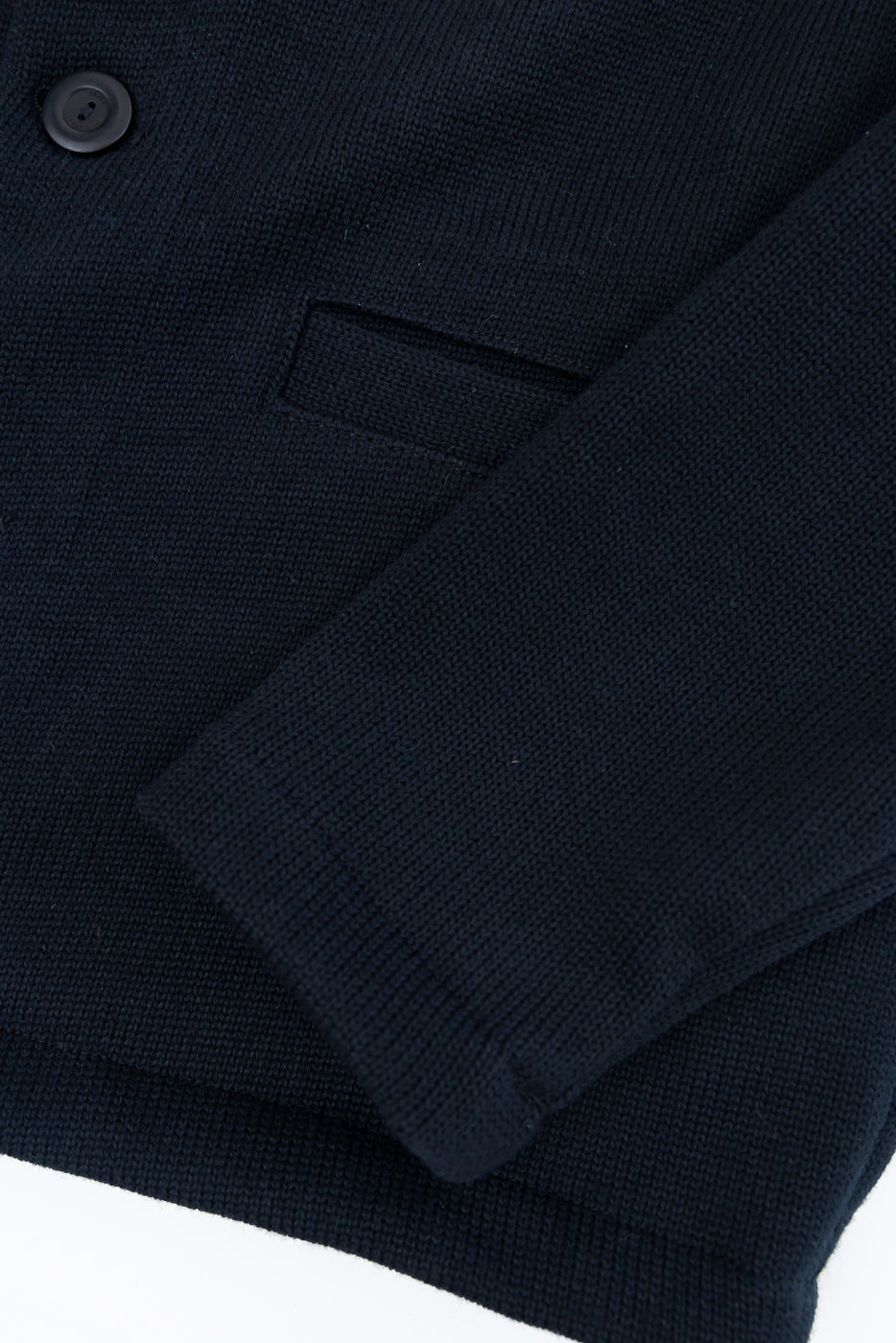 Close-up of a navy blue knit blazer front showing fabric texture, a button, and a pocket.