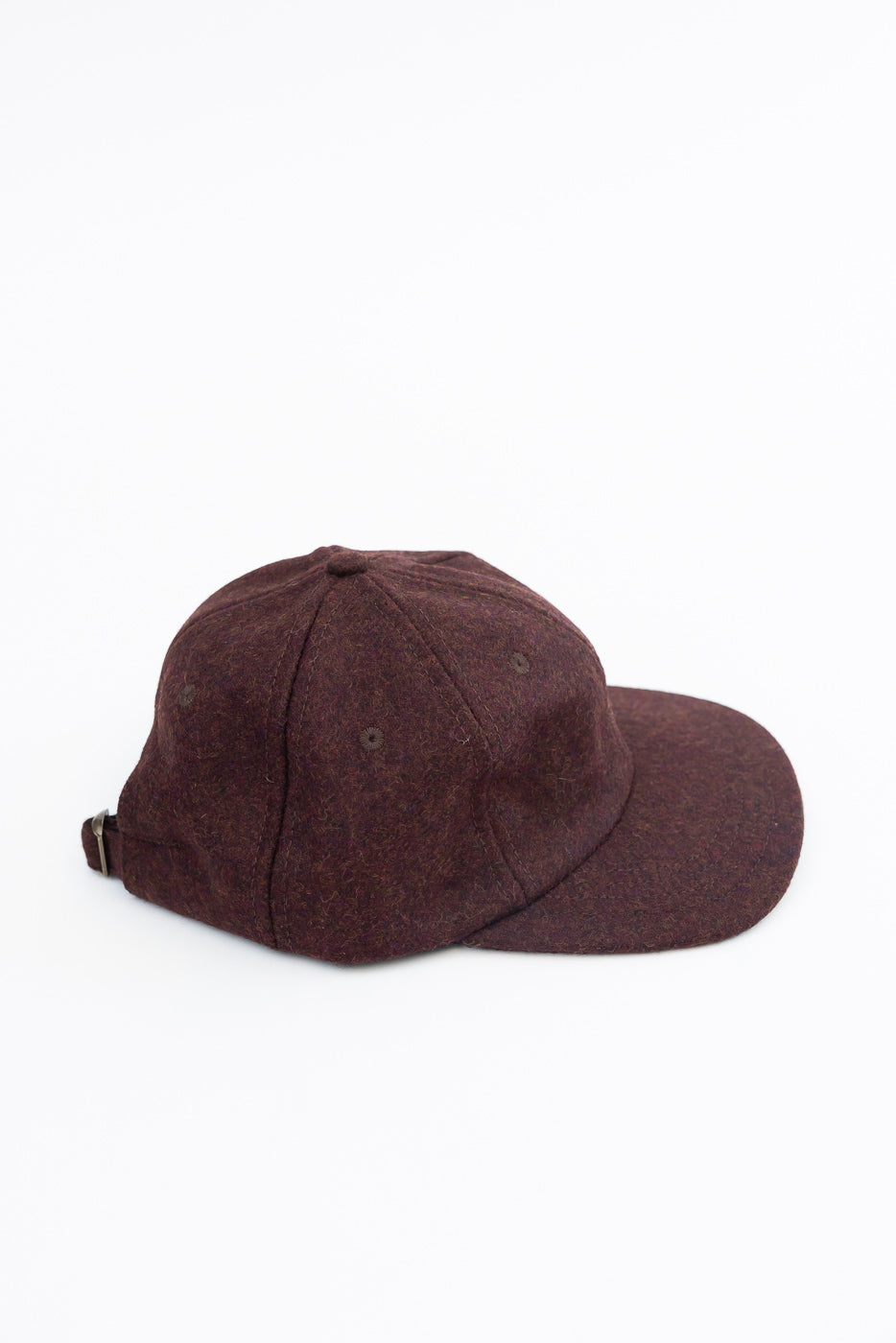 Close-up, side view of a burgundy wool baseball cap showing textured fabric and adjustable strap.