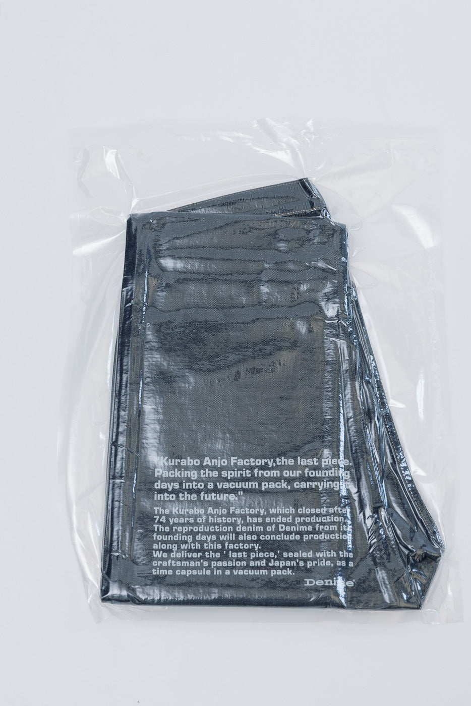 Back view of folded dark selvedge denim in a vacuum-sealed clear plastic package.
