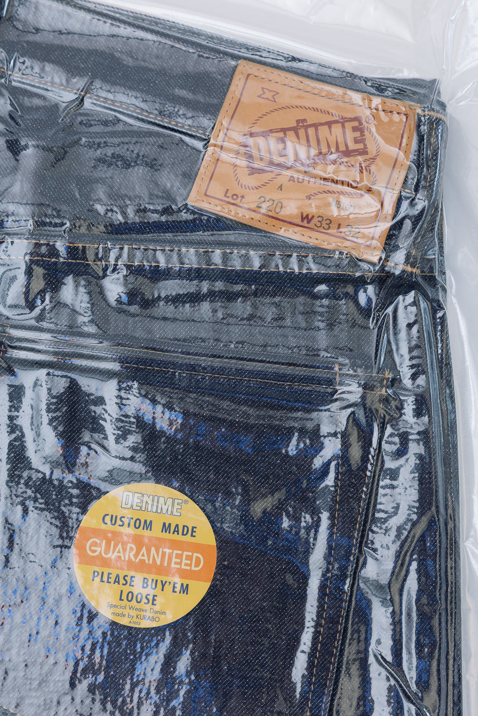 Close-up front view of dark selvedge denim fabric texture and leather waist patch.