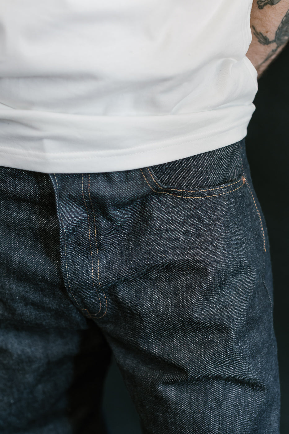 Person wearing blue jeans and a white shirt with a dark background