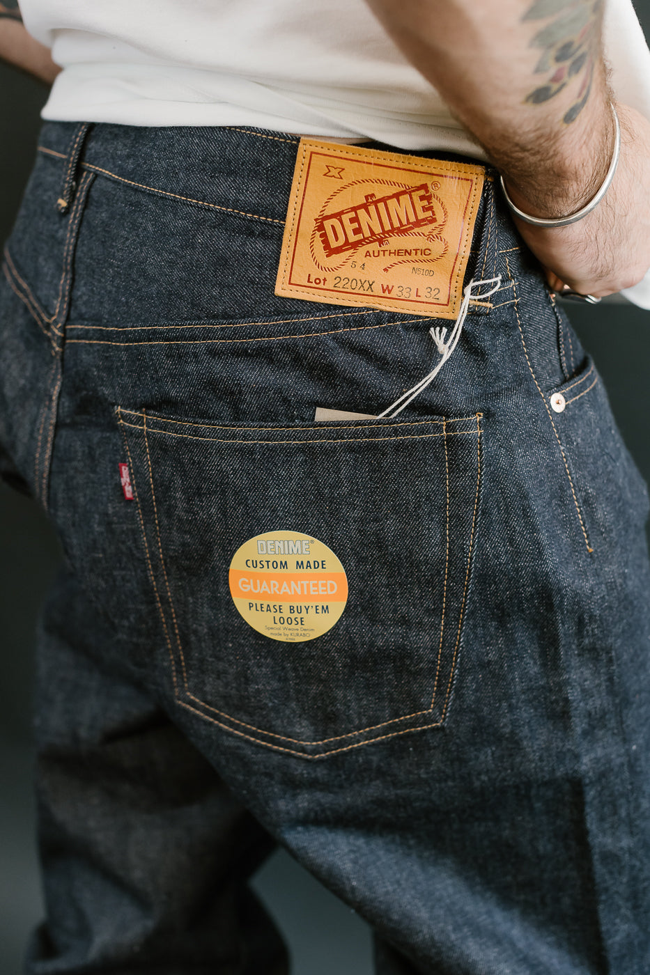Close-up of blue jeans with a 'Denim' brand label on the back pocket.