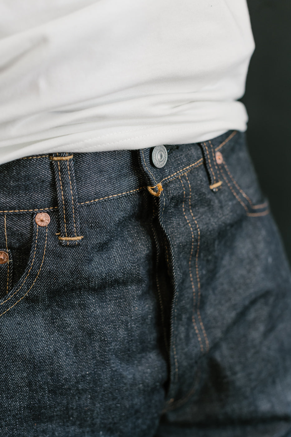 Close-up of blue jeans with a white shirt underneath on a dark background