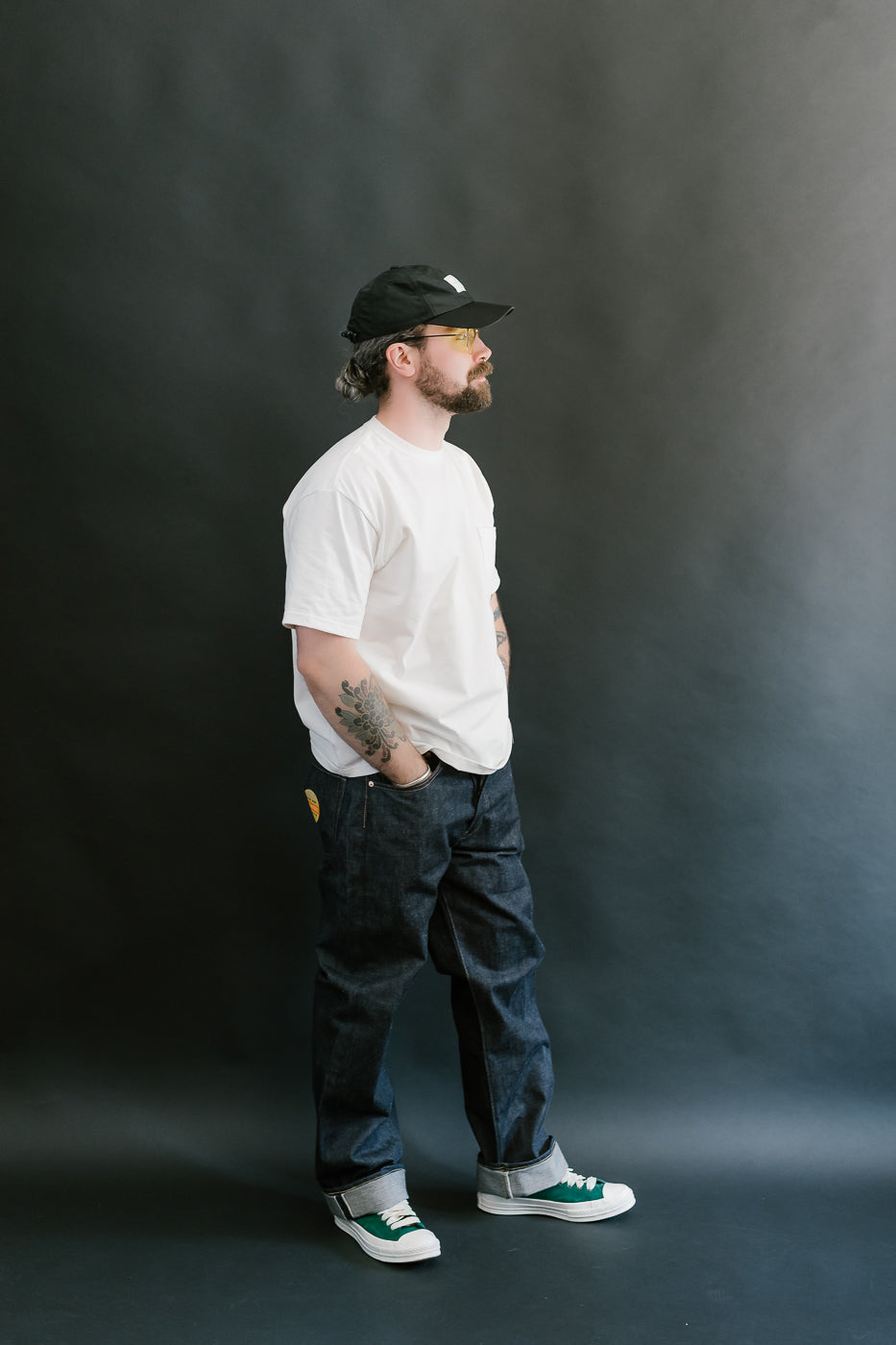 Man wearing a white t-shirt, dark pants, and a cap against a black background