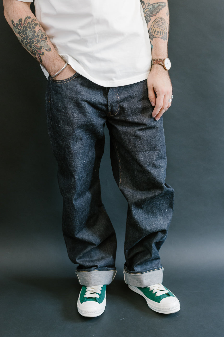Person wearing blue jeans and green sneakers against a dark background