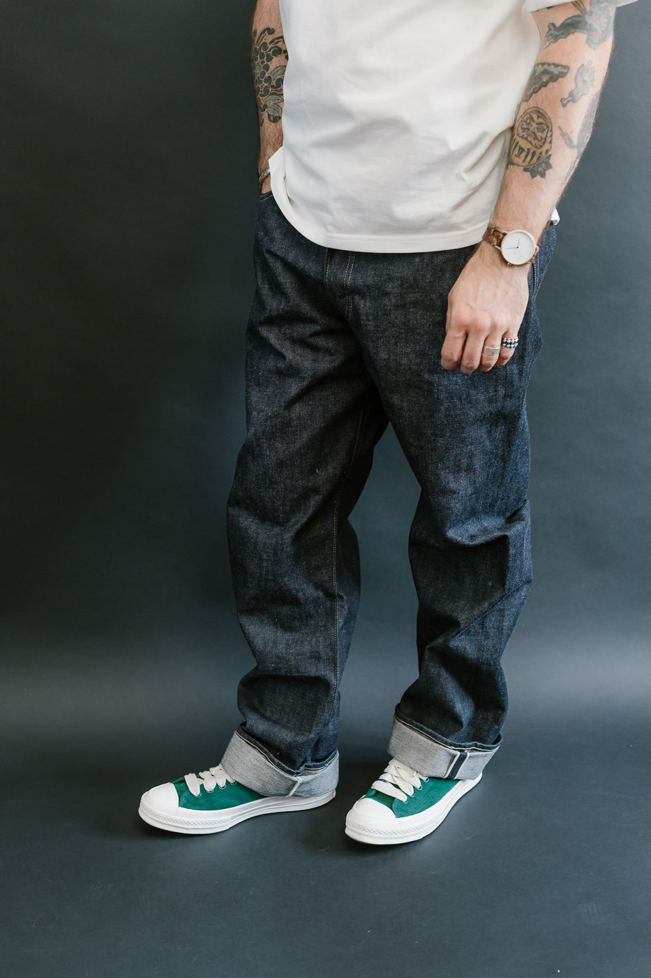 Person wearing dark jeans and white sneakers with green accents on a plain background