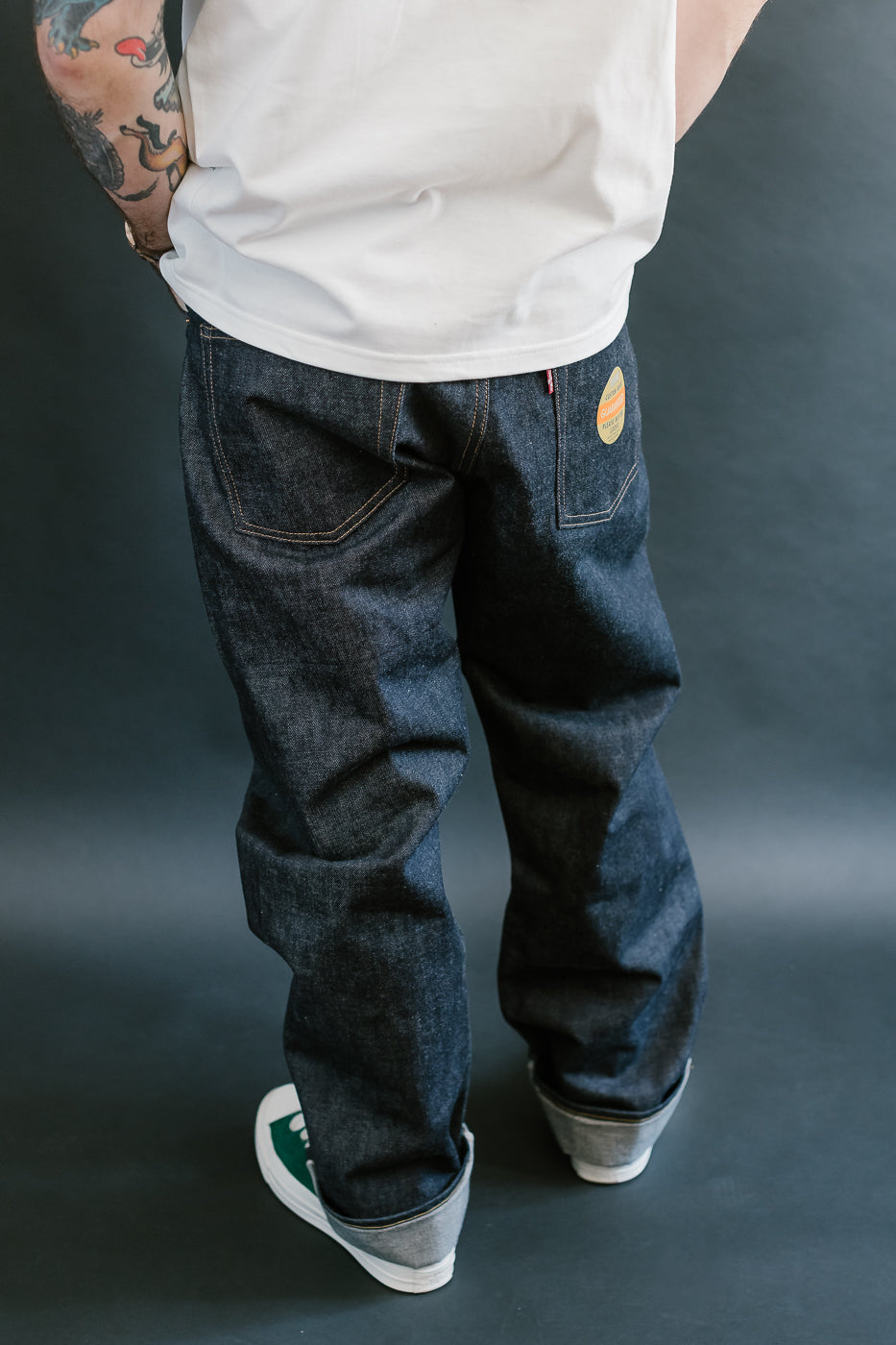 Person wearing dark blue jeans and a white tank top with a visible brand logo on a gray background