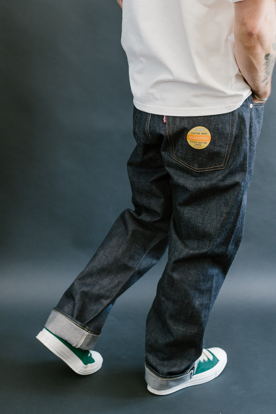 Person wearing dark jeans with a visible brand logo on a gray background