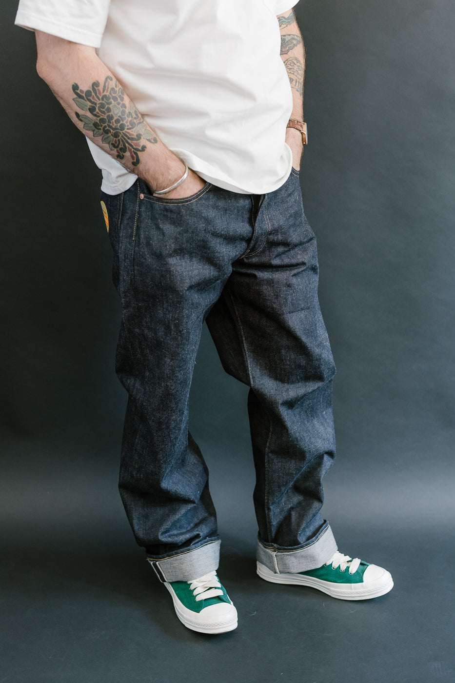 Person wearing a white t-shirt, dark jeans, and green sneakers against a gray background