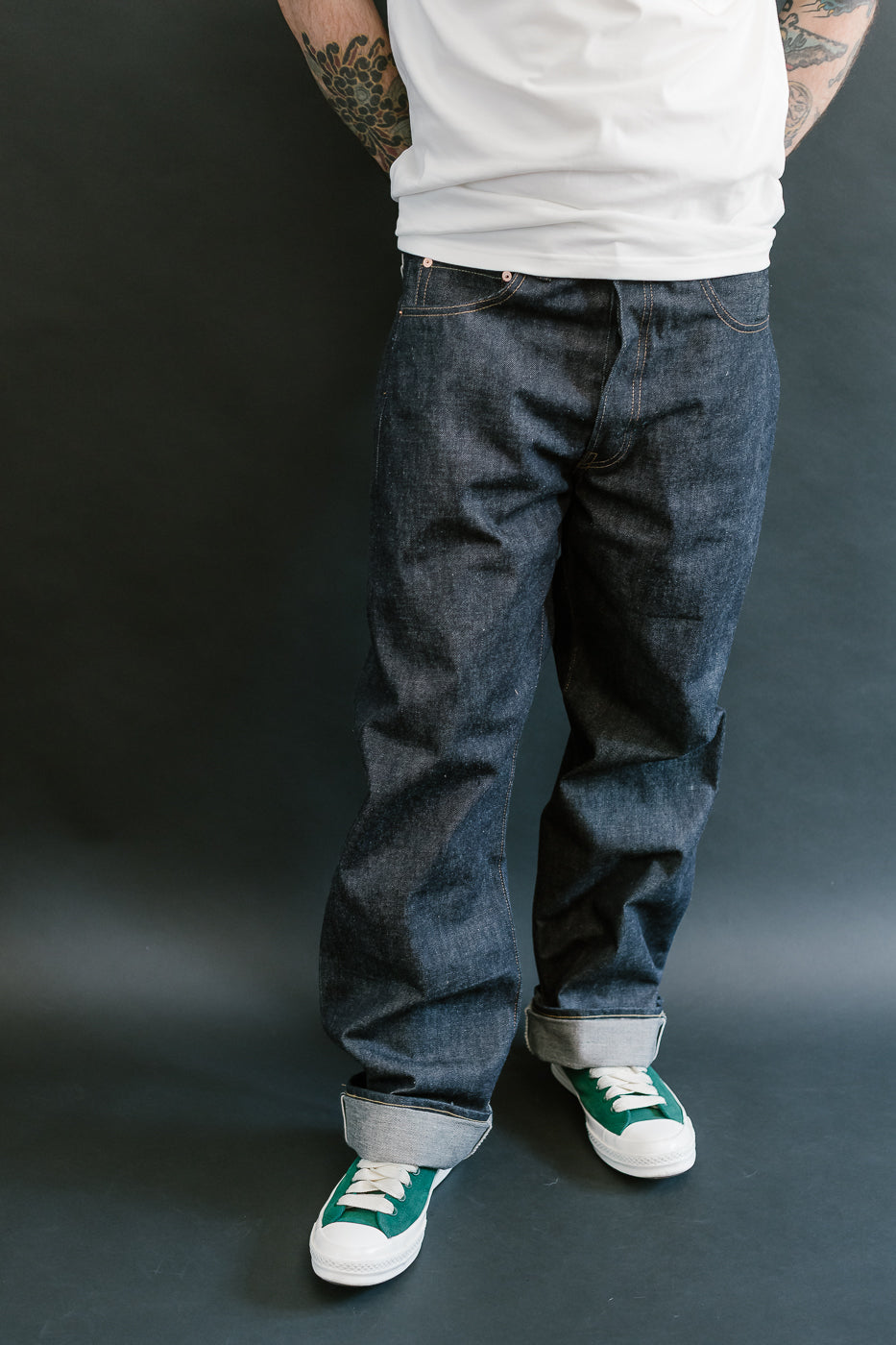 Person wearing dark blue jeans and green sneakers on a black background