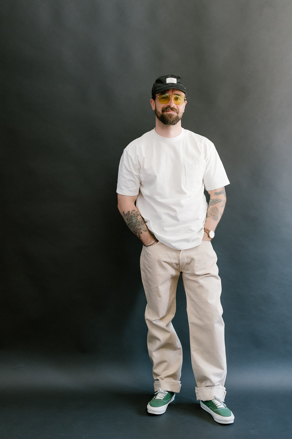 Man wearing a white t-shirt, beige pants, and green shoes against a dark background