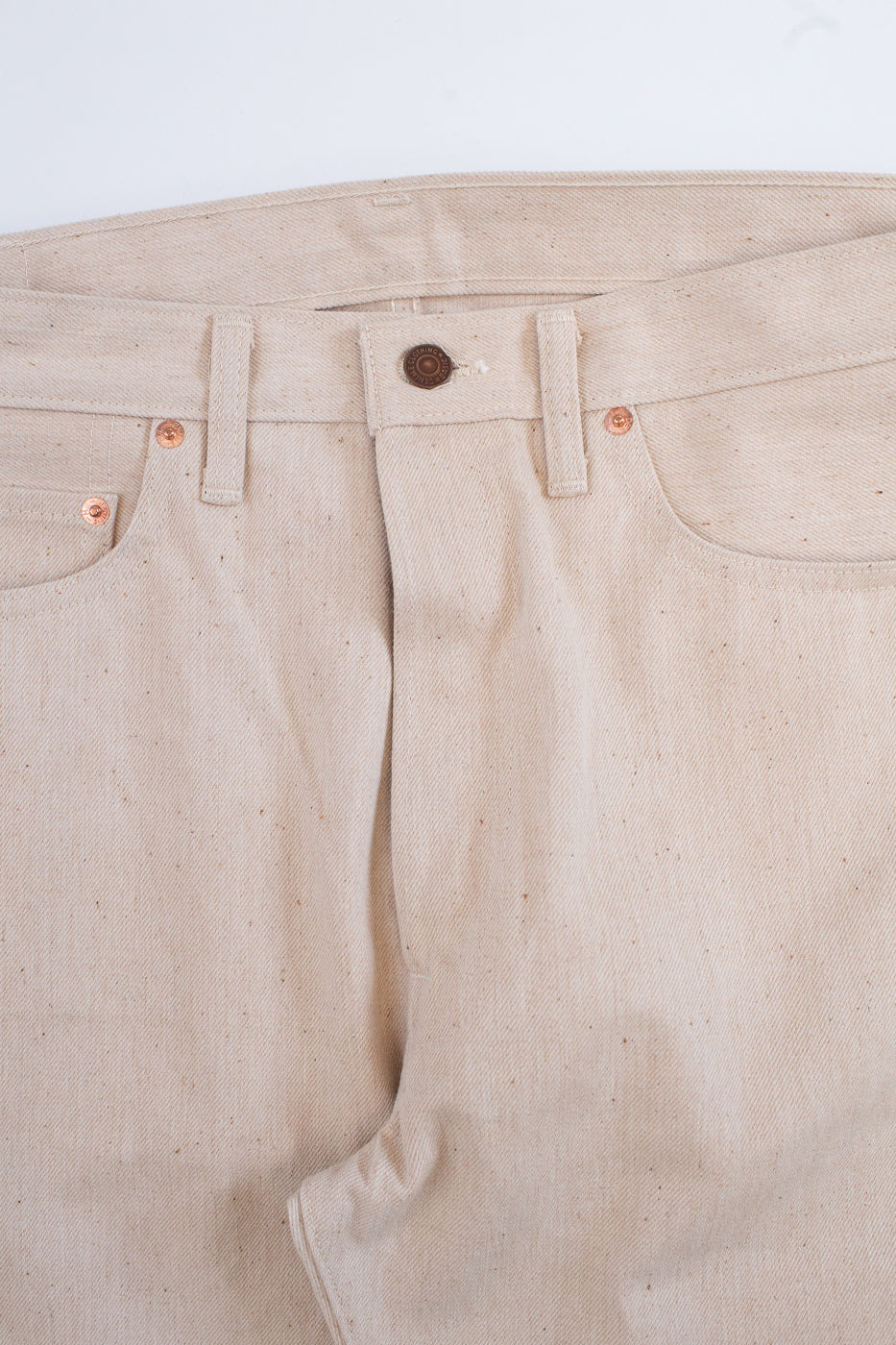 Close-up of beige pants with a button and stitching details on a light background