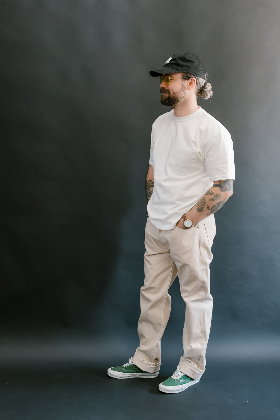 Man wearing a white t-shirt, beige pants, and green sneakers against a dark background