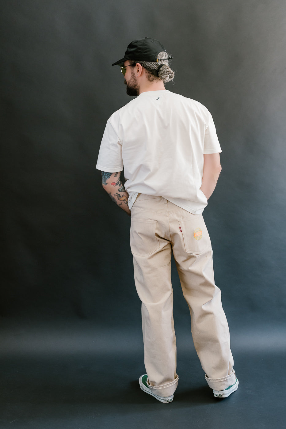 Man wearing a white shirt and beige pants against a dark background