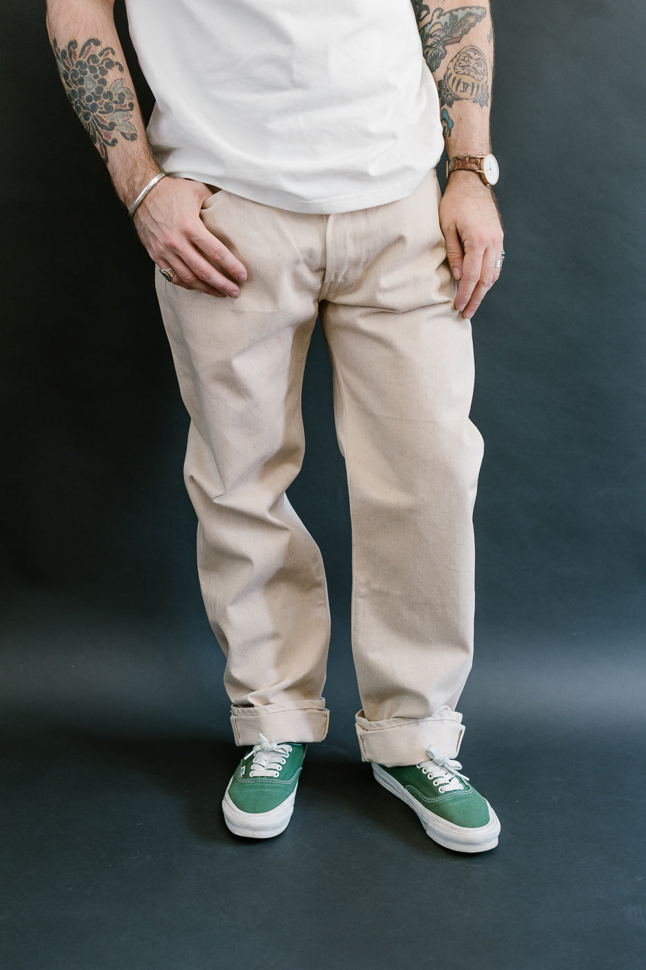 Person wearing beige pants and green sneakers against a dark background