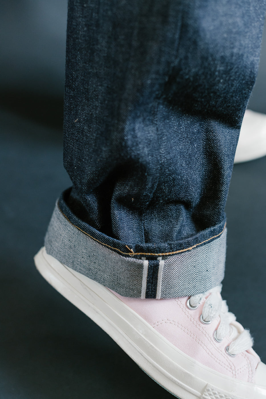 Close-up of dark blue jeans with a white sneaker on a blurred background