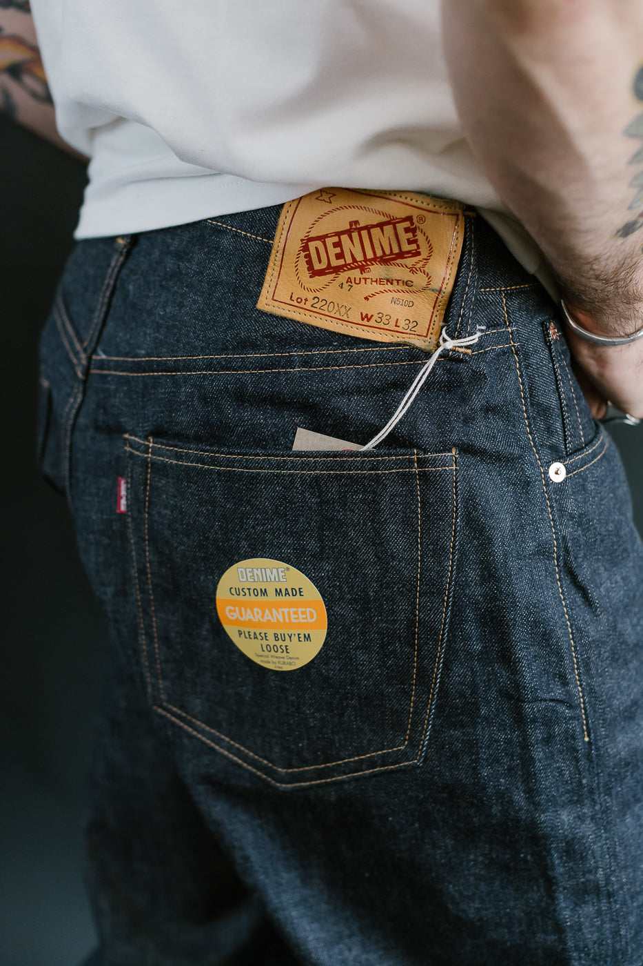 Person wearing dark blue denim jeans with visible brand labels on a dark background