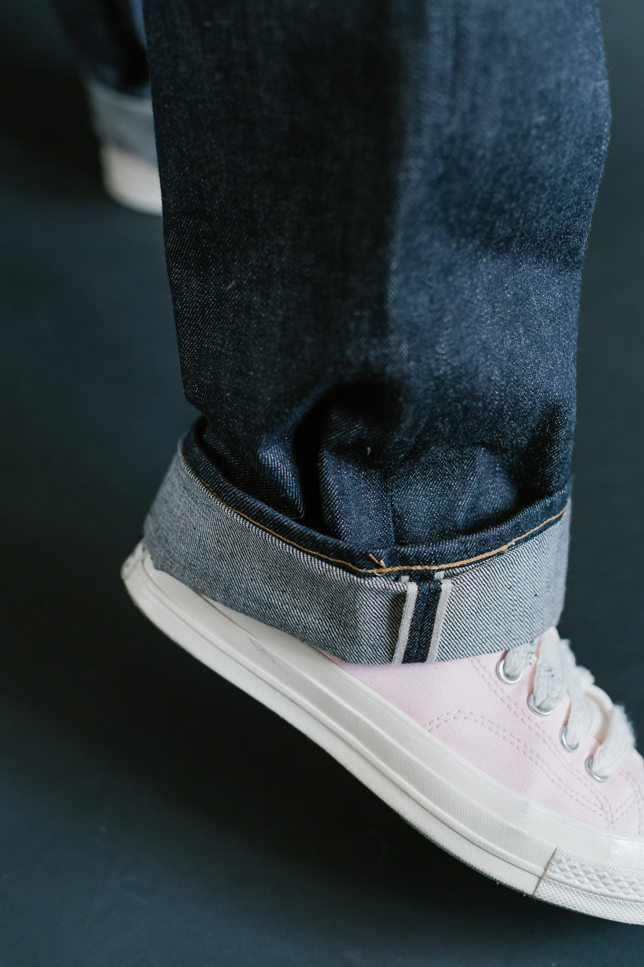 Close-up of a person wearing blue jeans and white sneakers on a dark background