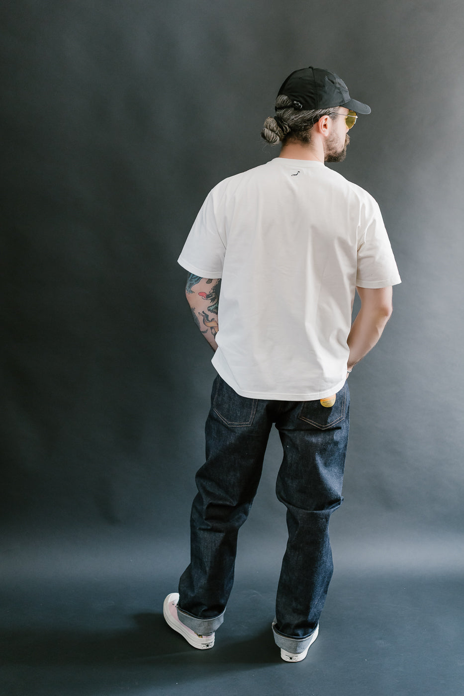 Man wearing a white t-shirt and black cap from behind on a gray background