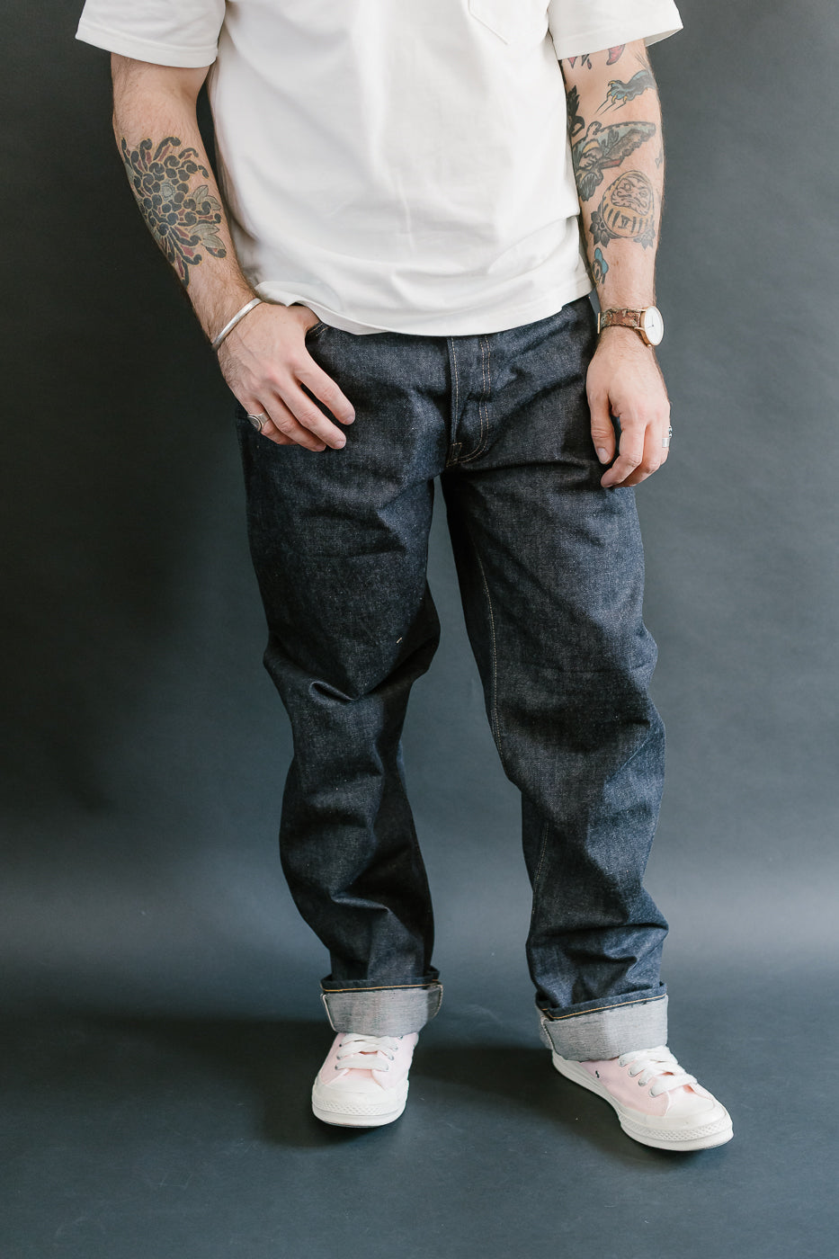 Person wearing dark jeans and white sneakers against a gray background