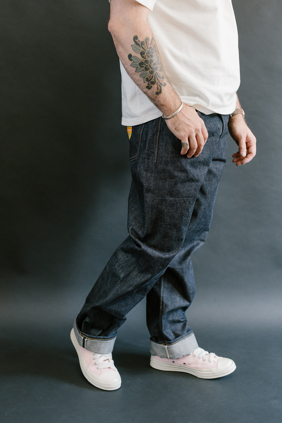 Person wearing dark blue jeans and white sneakers on a gray background