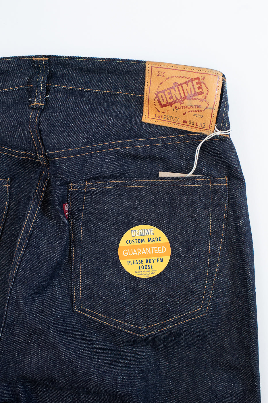 Close-up of a blue denim jeans with a brand label and authenticity sticker on a white background