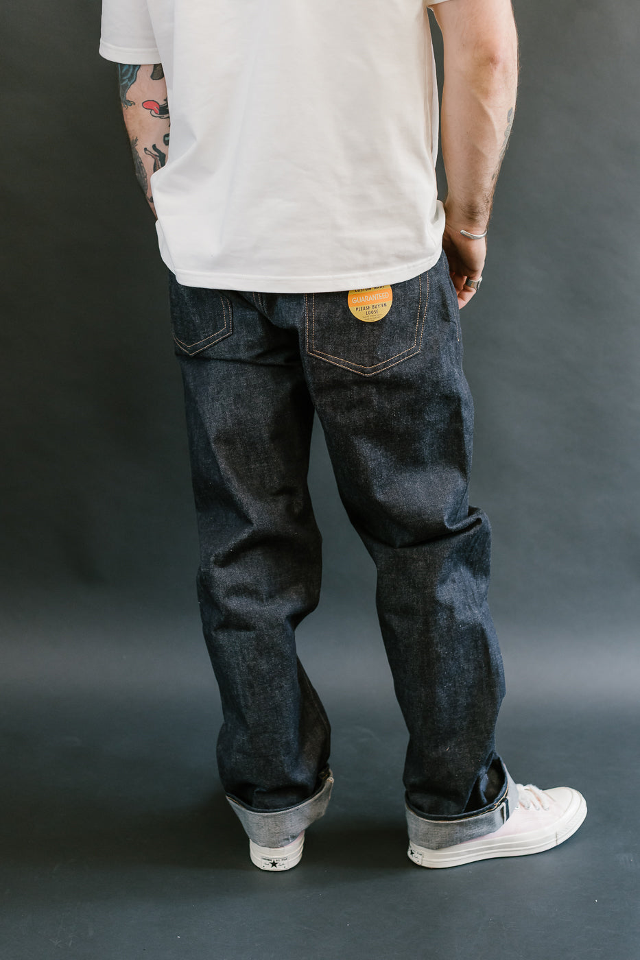 Person wearing dark blue jeans and a white t-shirt against a gray background