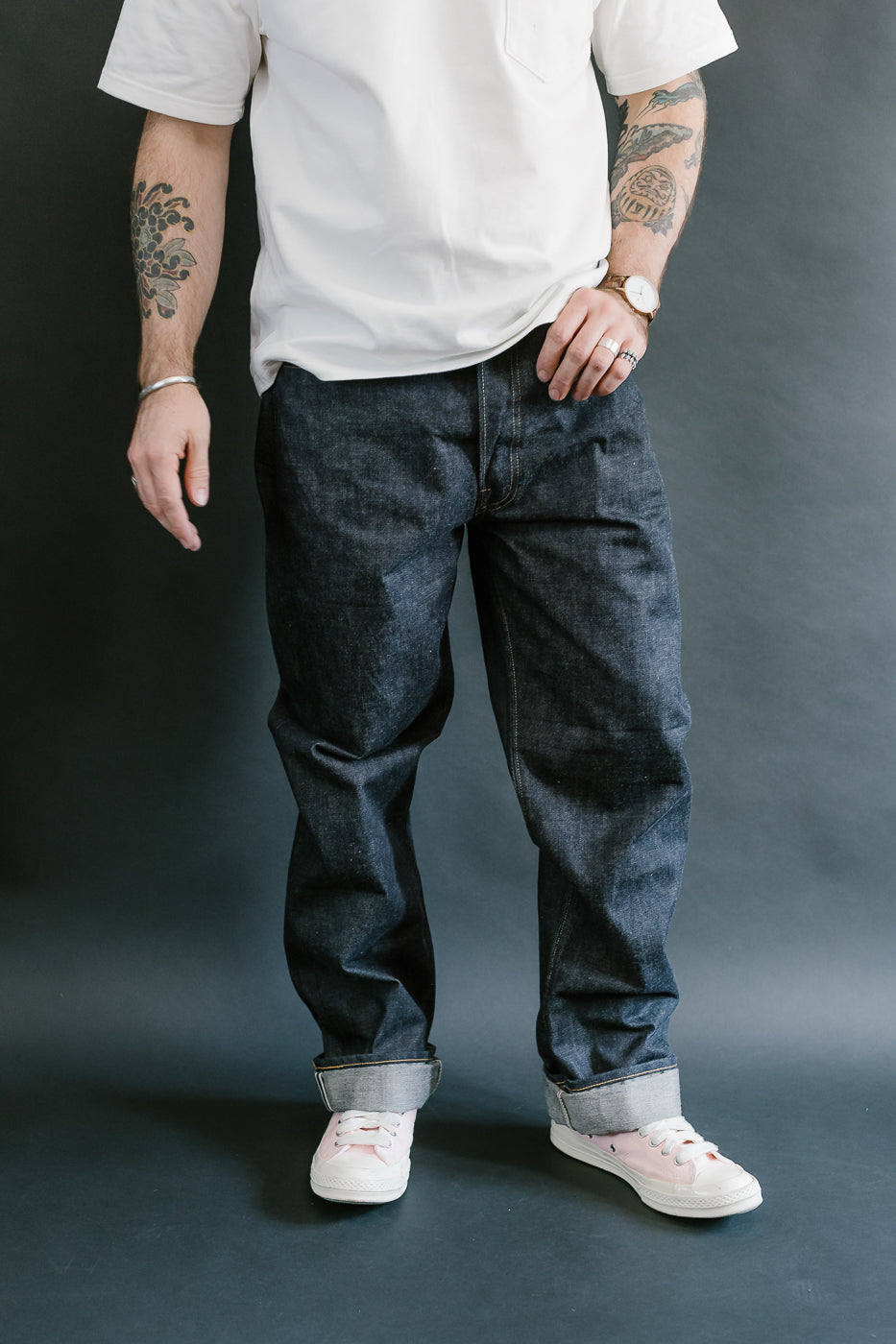 Person wearing a white t-shirt, dark jeans, and white sneakers against a gray background