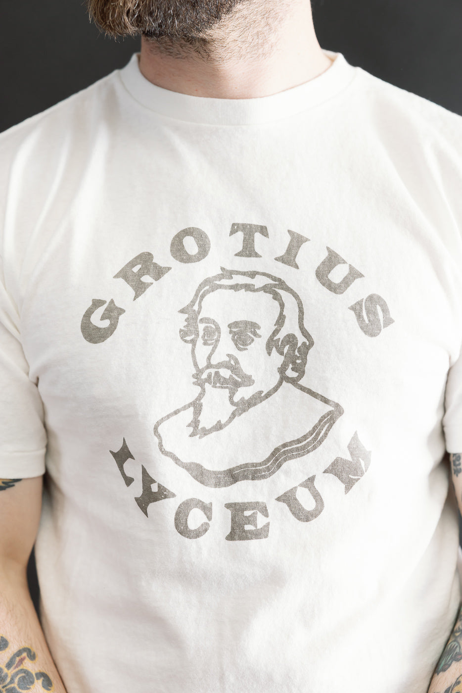 White T-shirt with a stylized line drawing of a 17th-century bearded figure encircled by “GROTIUS ACEUM,” showcasing the 5.4oz Raffy Tenjiku Printed T-Shirt Grotius - Off White.