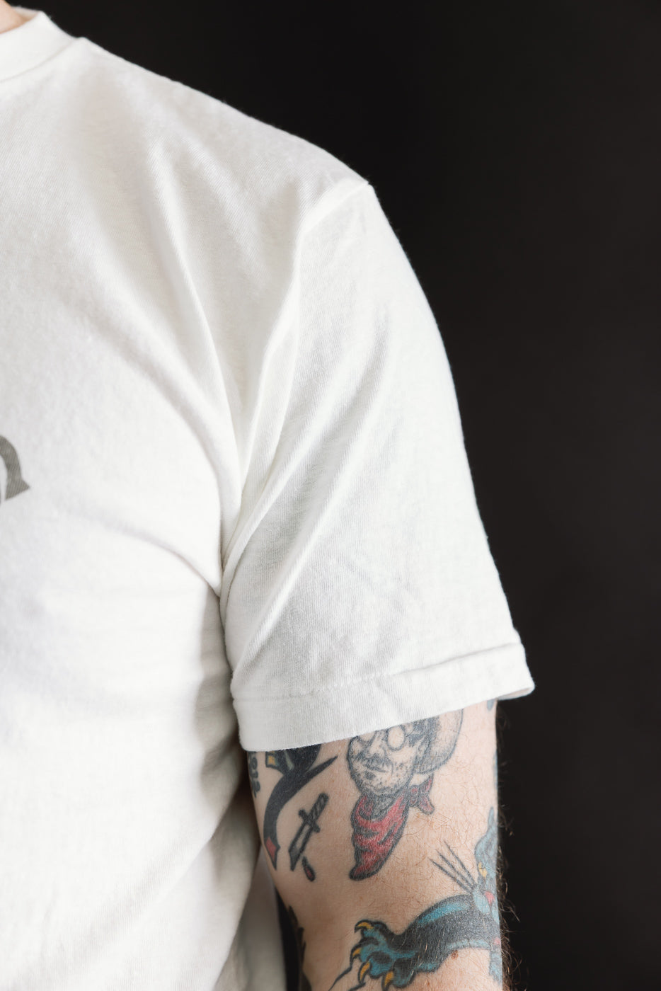 Person wearing the 5.4oz Raffy Tenjiku Printed T-Shirt Grotius in Off White, showcasing a smooth, tubular knit with no side seams, and featuring distinct tattoos on the forearm.