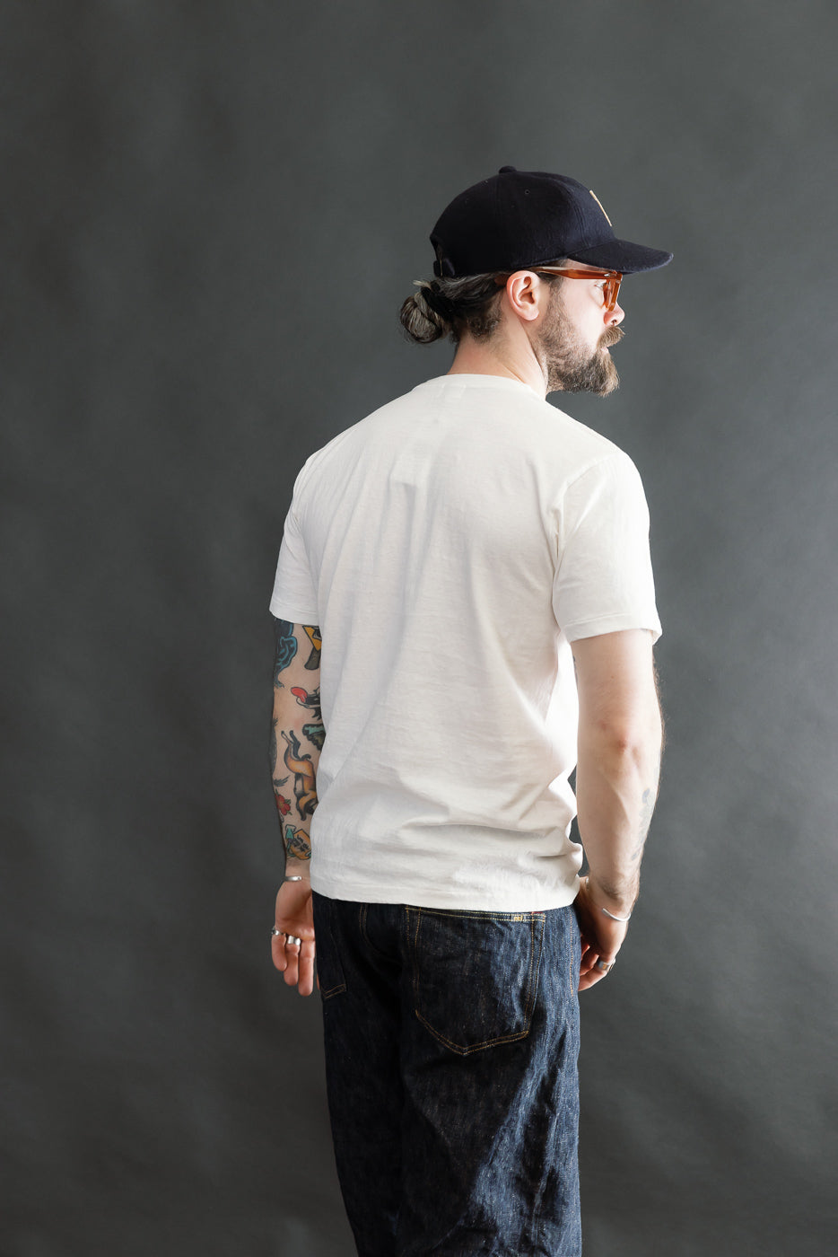 A man models the 5.4oz Raffy Tenjiku Printed T-Shirt Grotius in off white, showcasing its vintage-inspired design, clean tubular construction, and slub jersey texture, paired with dark blue jeans.