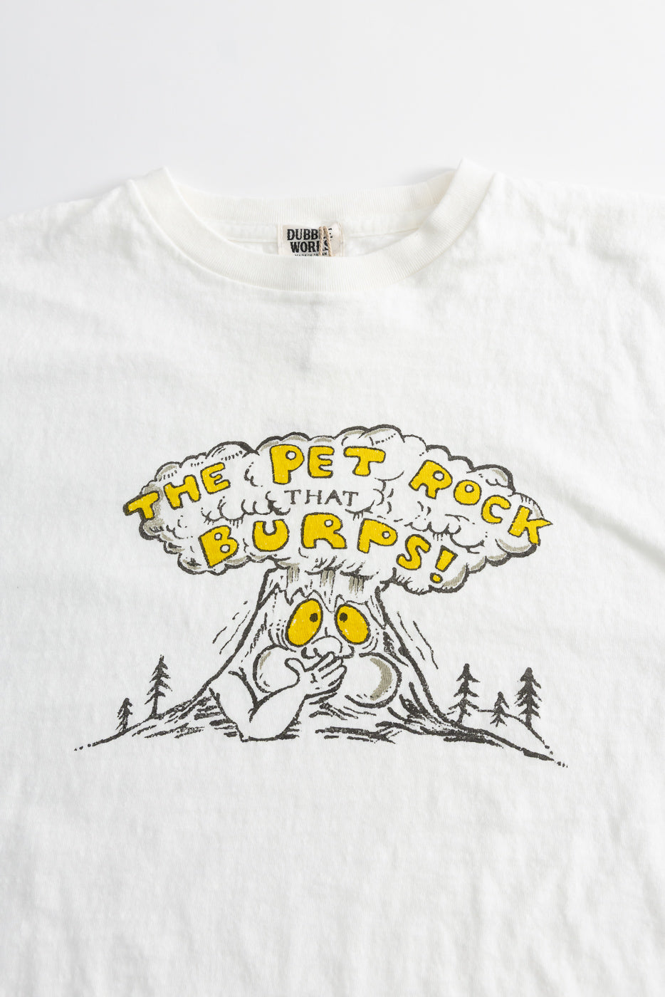 5.4oz Raffy Tenjiku Printed T-Shirt The Pet Rock features a cartoon volcano resembling a pet rock with eyes, burping a mushroom cloud, and the phrase “THE PET ROCK THAT BURPS!” in yellow above.