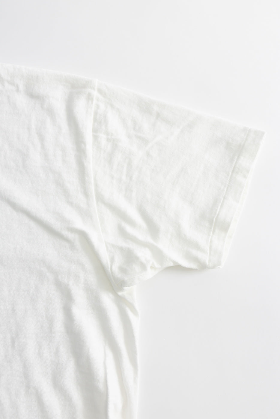 Close-up of the 5.4oz Raffy Tenjiku Printed T-Shirt The Pet Rock - Off White, highlighting the sleeve and upper torso area, showcasing the vintage-inspired slub jersey texture and seamless tubular knit construction.