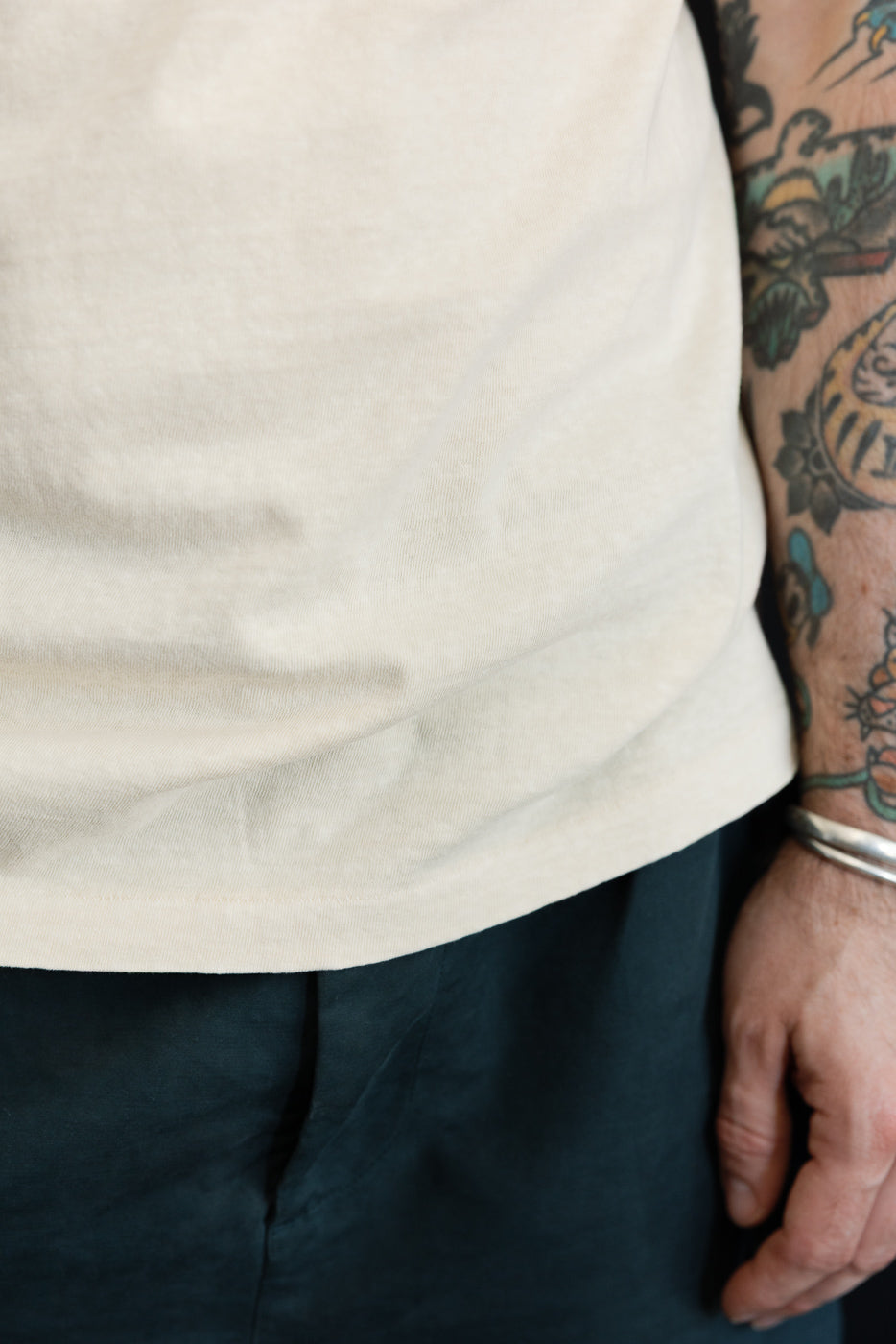 Close-up side view of male model’s off-white tee hem and dark shorts, showcasing fabric texture and fit.