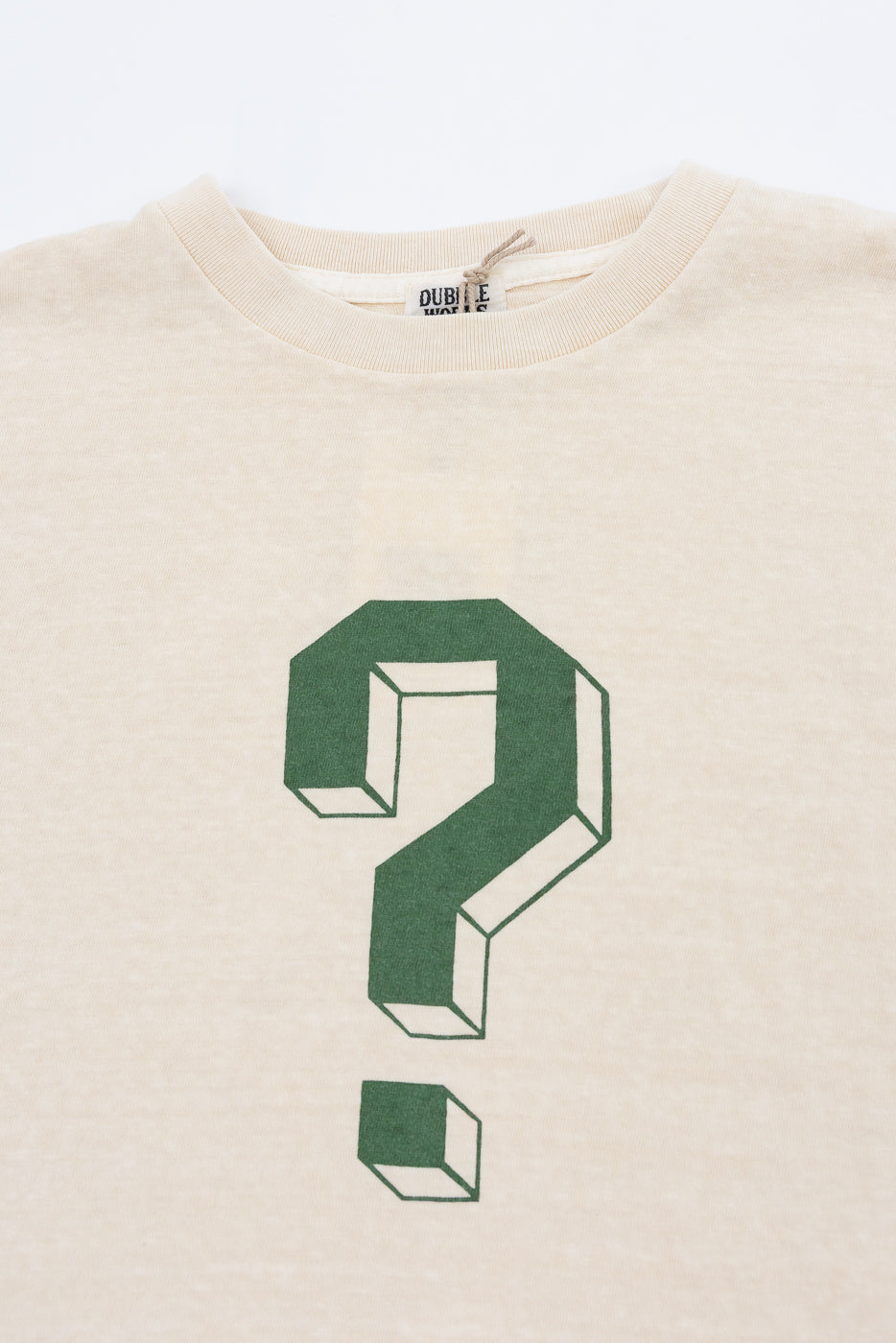 Close-up front of beige tee with green 3D question mark graphic, ribbed collar, and tag detail