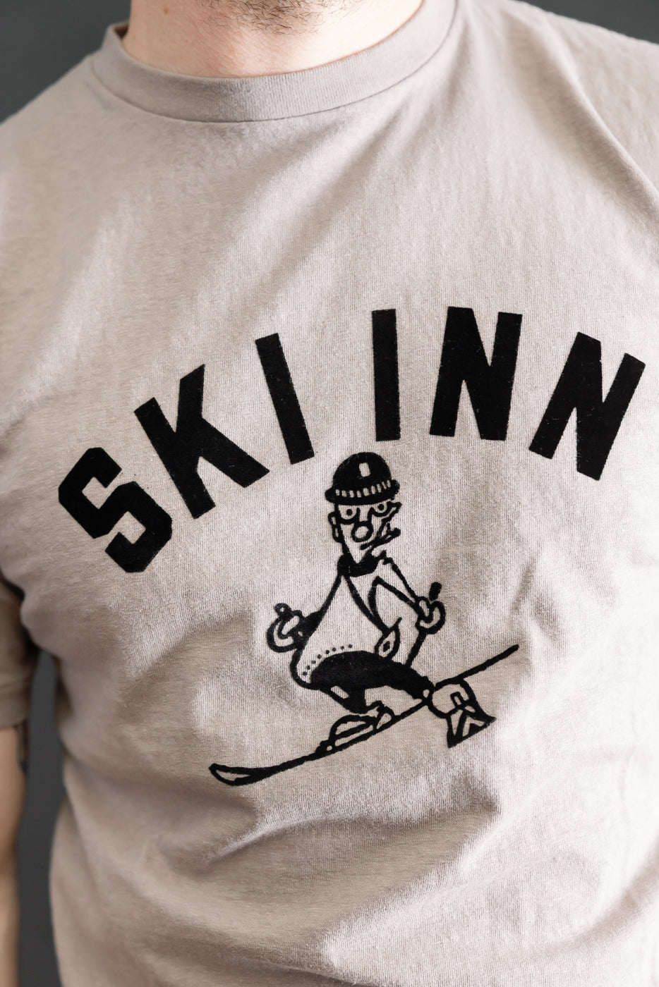 5.4oz - Raffy Tenjiku Printed T-Shirt Ski Inn - Grey, featuring bold black SKI INN lettering and a cartoon skier graphic, highlighting its vintage-inspired style and superior Japanese craftsmanship.