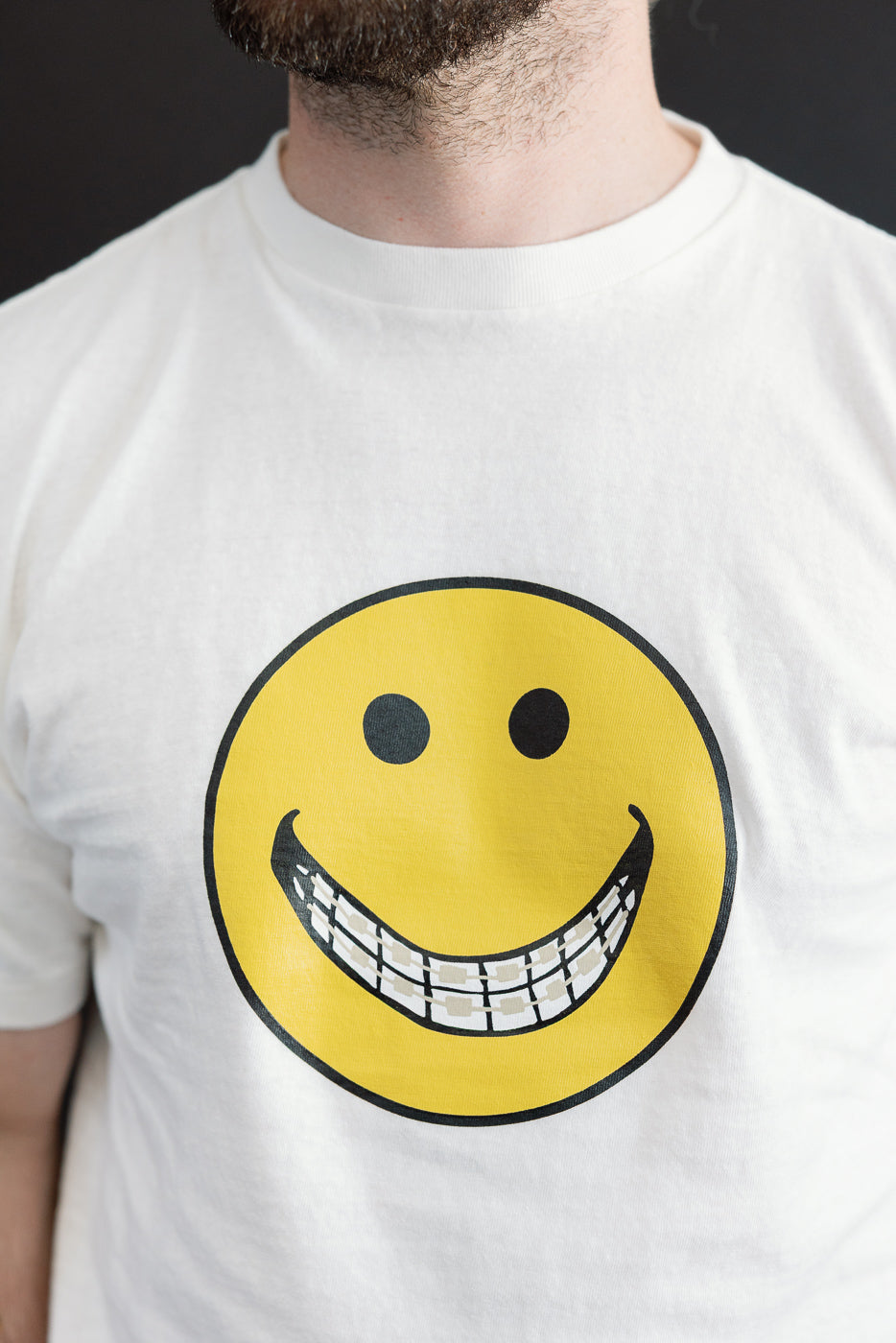 Close-up front view of a white t-shirt with a smiley face graphic on a 5'9