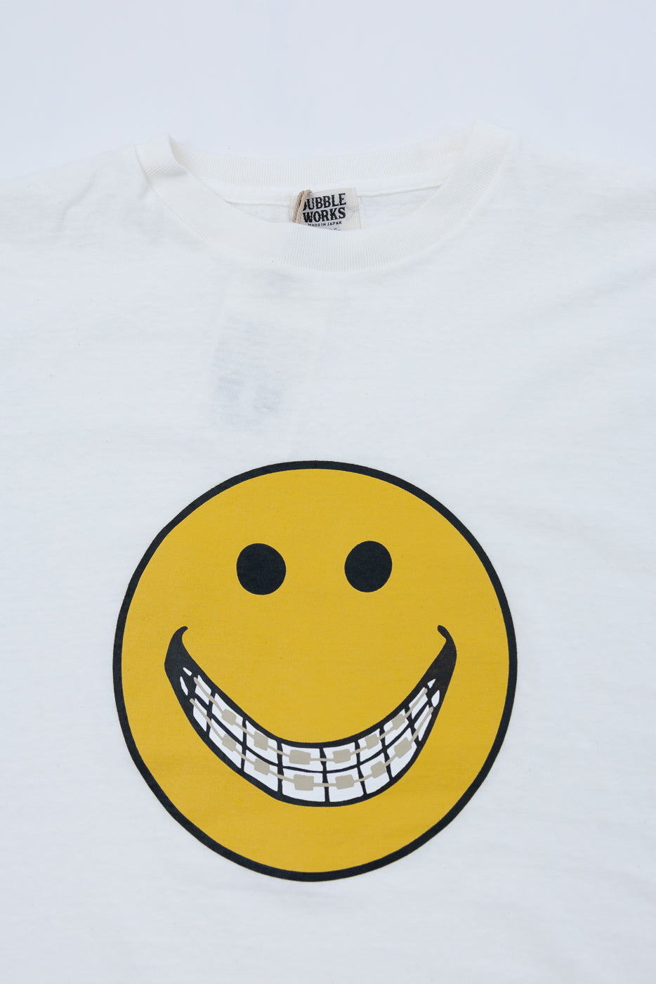 Close-up of the front of a white t-shirt featuring a smiley face graphic and a neck tag.