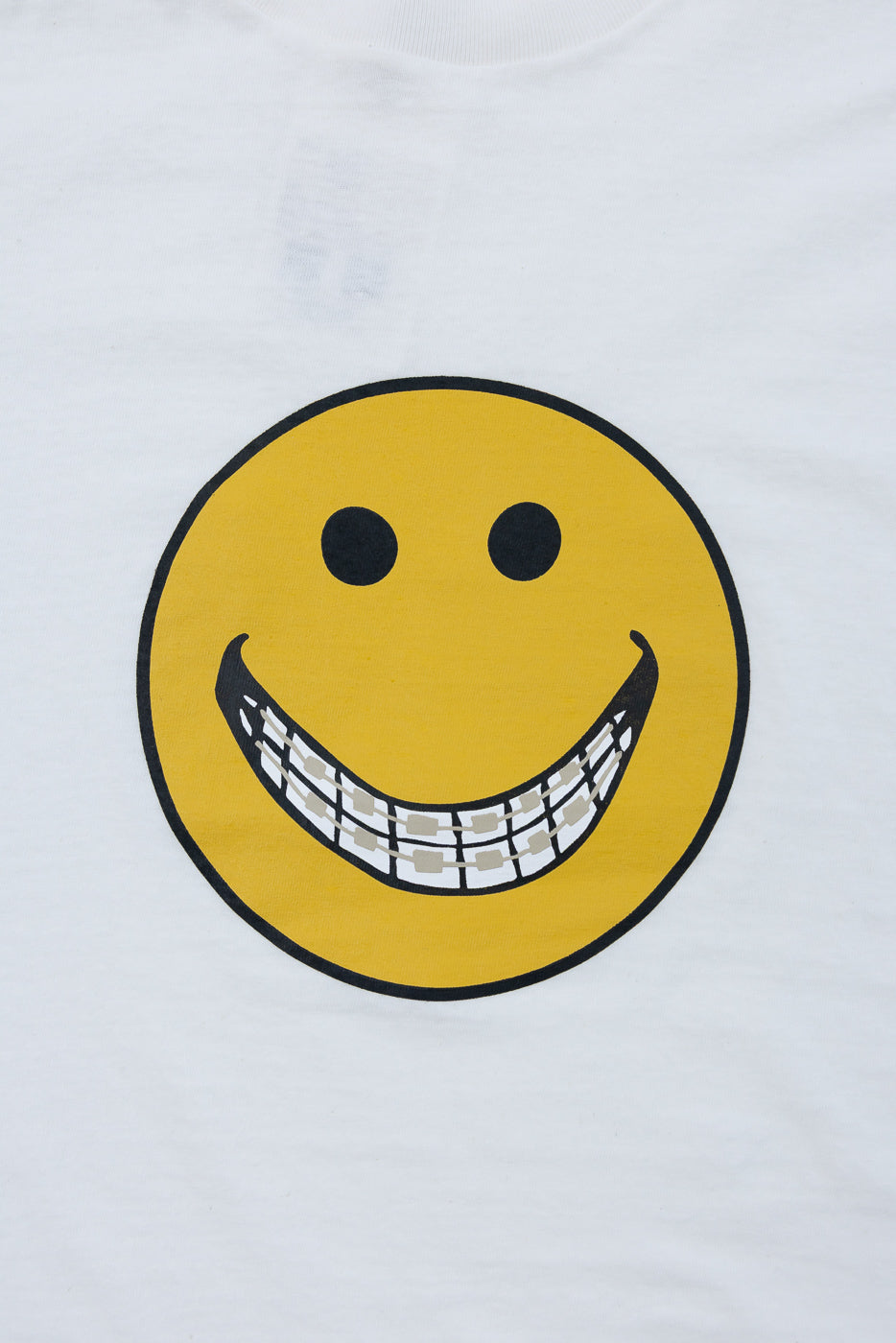 Close-up of the front of a white t-shirt featuring a yellow smiley face with a grill graphic.