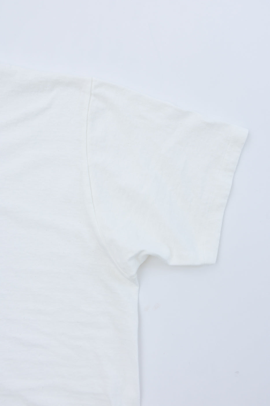 Close-up flat lay of the right sleeve and side of a white t-shirt.