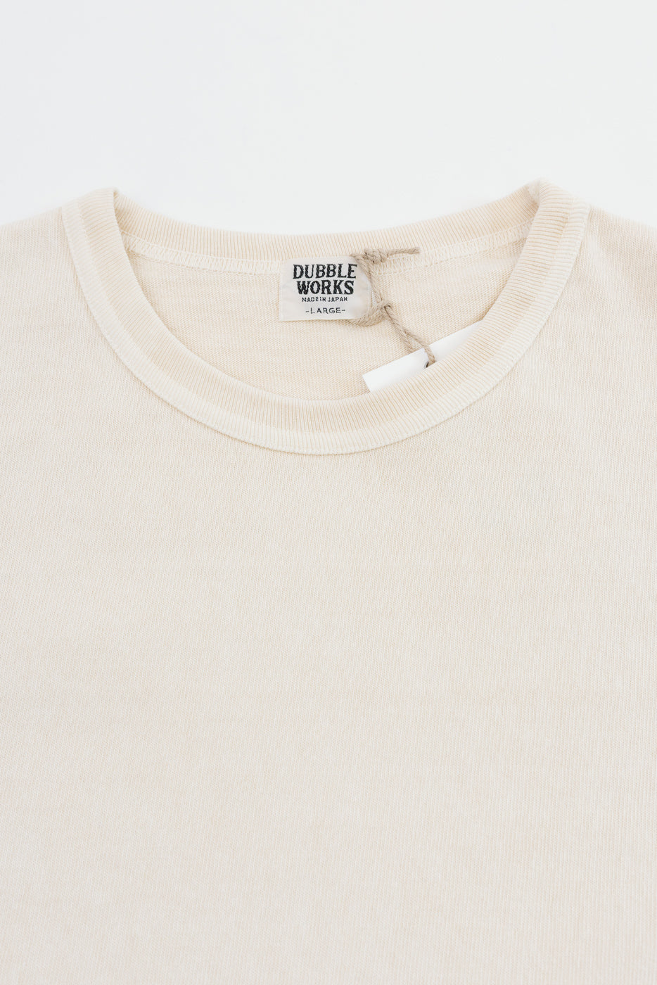 Close-up of cream t-shirt collar with Dubble Works tag, showing fabric texture and neckline detail