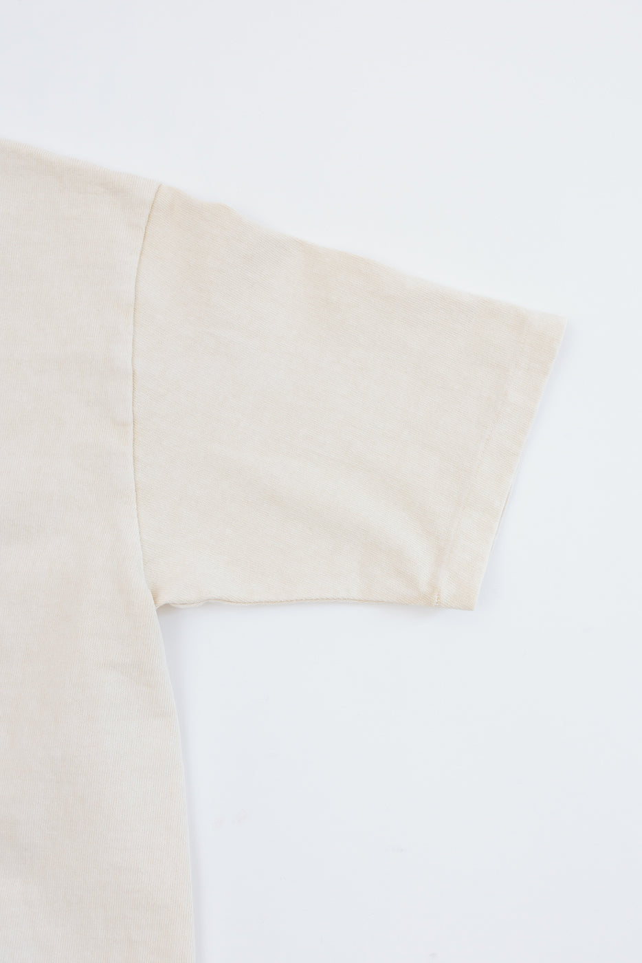 Close-up of cream t-shirt sleeve and shoulder seam, showing fabric texture and clean hem detail