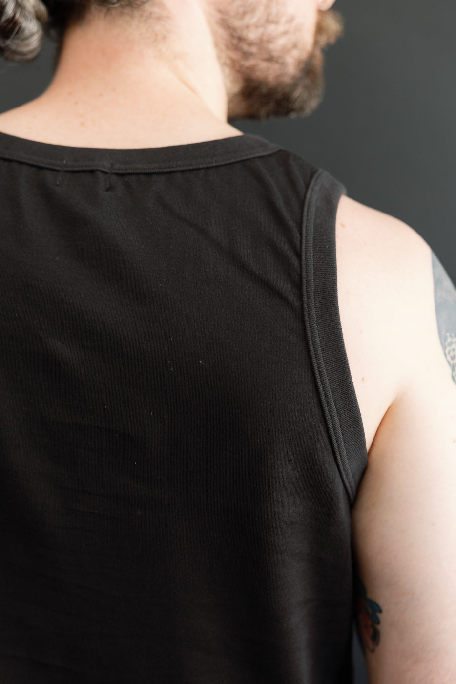 Back view of black tank top on male model, 5'9