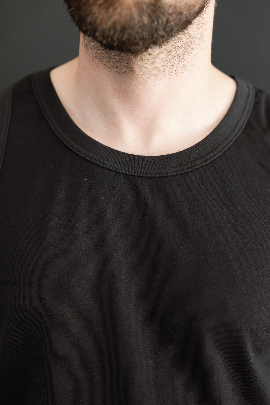 Close-up front view of black crewneck tee on male model, showcasing ribbed collar and fabric texture.